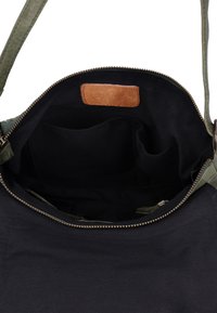 Borsa in tessuto nera aperta con chiusura a zip, manici verde oliva e etichetta interna in pelle marrone visibile all'interno.