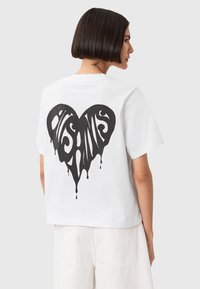 Hvid bomulds t-shirt med et stort sort drippende hjerte design på ryggen. Korte ærmer og en afslappet pasform.