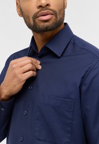 Dunkelblaues Hemd mit strukturierter Oberfläche, Button-Down-Kragen und einer Brusttasche. Verfügt über passende Knöpfe und ist tailliert für einen figurbetonten Look.