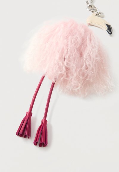 Ροζ αφράτο μπρελόκ με δύο σκούρες ροζ δερμάτινες φούντες και μεταλλικό κούμπωμα προσαρτημένο σε μικρό γκριμπιέ σε σχήμα παπουτσιού μπεζ και μαύρου χρώματος.