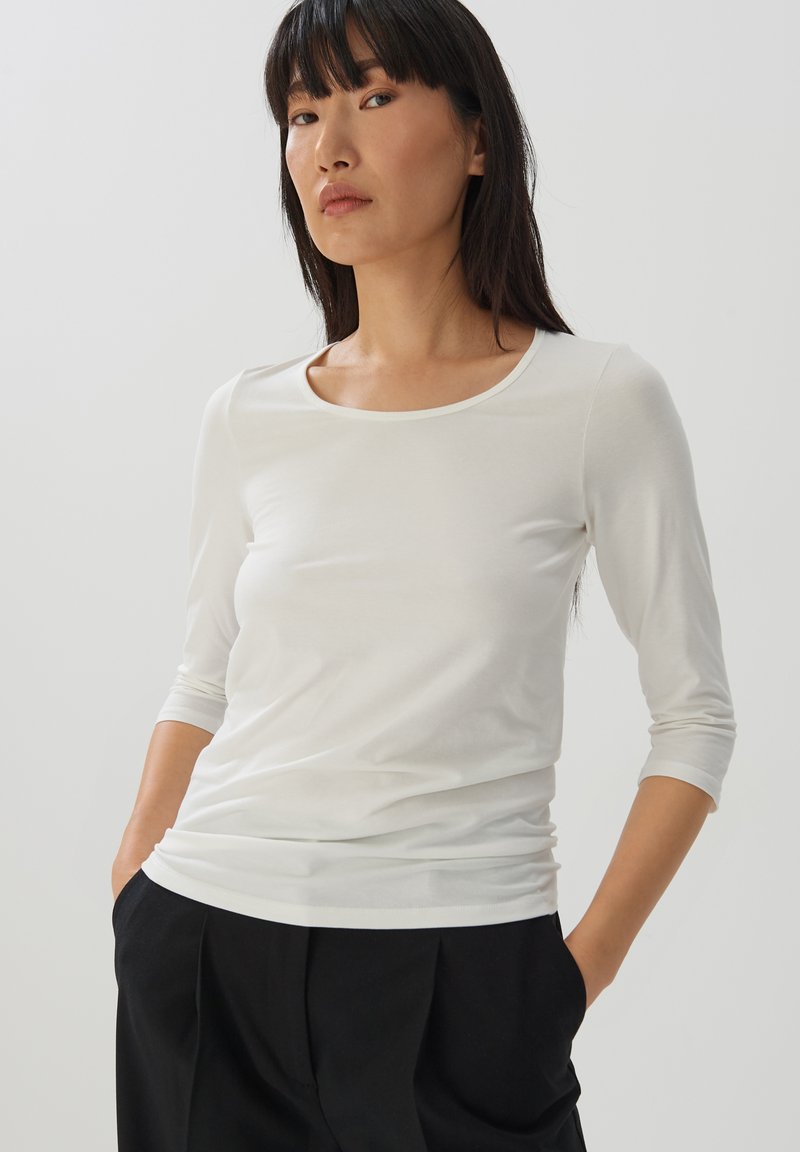 Weißes, tailliertes Langarmshirt mit Rundhalsausschnitt und glattem, leichtem Stoff. Das Shirt hat dreiviertellange Ärmel und ein nahtloses Design.