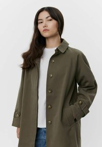 Trench coat verde oliva con colletto, sei bottoni sul davanti e tasche laterali. Presenta una vestibilità comoda e una texture liscia.