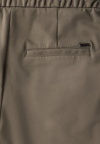 Khaki tapers met een soepele stoffen textuur, voorzien van een elastische tailleband en een klein achterzakje met een subtiele merketiket.