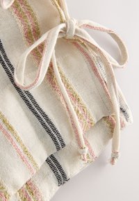 Close-up of beige fabric with pink, olive, and black woven stripes and a tied drawstring with knots at the ends.