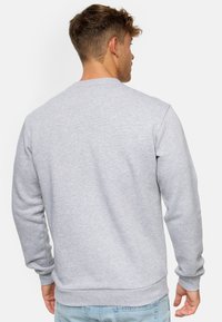 Sudadera gris claro hecha de tejido suave, con mangas largas, cuello redondo y puños y dobladillo de canalé, mostrada desde la parte trasera.