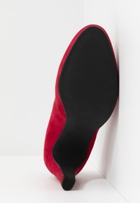 Chaussure à talon aigu en daim rouge avec un bout pointu et une semelle en caoutchouc noir texturé, présentée avec la semelle vers le haut. Taille indiquée comme 37.