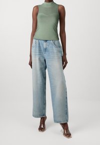 Grøn udenærmet top med ribbet design, parret med lyseblå brede jeans. Klare hælede sandaler fuldender outfittet.