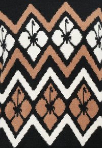Strickpullover mit einem geometrischen Muster in Schwarz, Weiß und Beige, verziert mit floralen Motiven und Zickzackakzenten in einem strukturierten Material.