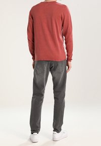 Maglietta rossa a maniche lunghe con scollo tondo, abbinata a jeans grigi. Il look è completato da sneakers bianche con dettagli verdi.