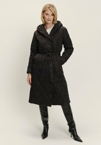 Prešívaný čierny dlhý kabát s kapucňou, opaskom v páse a gombíkovým zapínaním, s textúrovaným diamantom a bočnými vreckami.