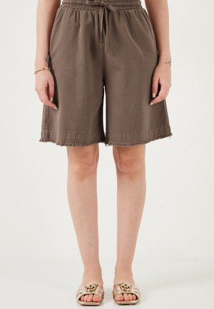 Pruunid põlveni ulatuvad lõdvalt paelaga reguleeritavad lühikesed püksid, mille äär on hästi kulunud, seljas seisva inimese seljas, kombineeritud beežide avatud varbaga sandaalidega, millel on kuldsed kettid.