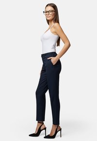 Marynarskie spodnie o dopasowanym kroju, z kieszeniami z przodu i eleganckim stylem. Połączone z czarnymi szpilkami w szpic i białą koszulką bez rękawów.
