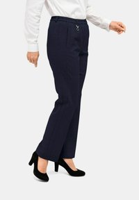 Marineblaue maßgeschneiderte Hose mit strukturiertem Design, elastischem Bund, Fronttaschen und silbernem Akzent. Getragen mit schwarzen High Heels.