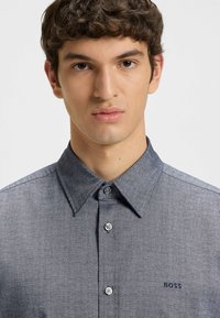 Overhemd met knopen in donkerblauwe textuurstof, voorzien van een spread collar, zes knopen en een klein "BOSS" logo op de borst.