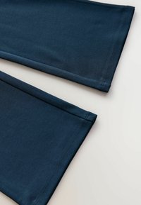  marineblaue Stoffleggings mit glatter Textur, flachen Säumen und genähten Details entlang der Ränder.