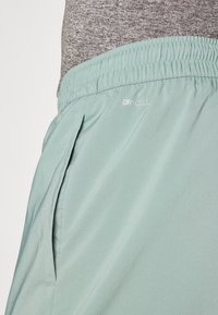 Light green athletic shorts with an elastic waistband, featuring side pockets and a "DRYCELL" label near the waistband. Smooth, lightweight fabric.