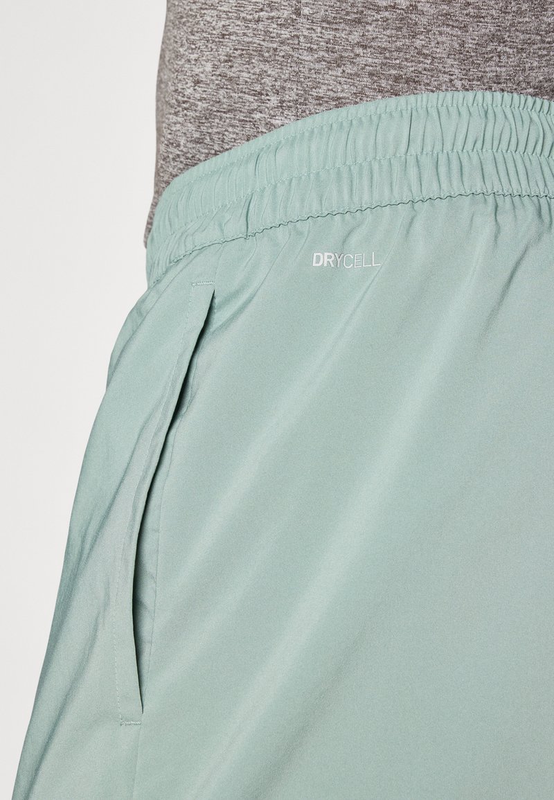 Hellgrüne Sportshorts mit elastischem Bund, ausgestattet mit Seitenreißverschlusstaschen und einem "DRYCELL"-Label in der Nähe des Bundes. Durch das glatte, leichte Material besonders bequem.