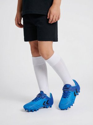Dziecko noszące czarne spodenki, białe podkolanówki oraz niebieskie korki piłkarskie z czarnymi akcentami, stojące na białym tle.
