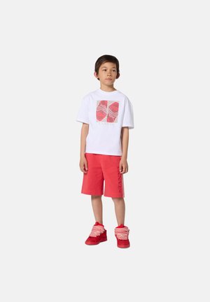 T-shirt blanc avec un motif graphique rouge, associé à un short rouge avec des accents latéraux. Baskets montantes rouges avec des détails texturés.