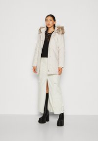 Doudoune blanche avec capuche en fausse fourrure, associée à un haut en dentelle noir et une jupe cargo crème. Des bottes à plateforme noires complètent l'ensemble.