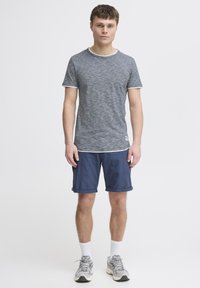 Tricou pe gri și alb cu dungi, cu mâneci scurte și gât rotund, asociat cu pantaloni șort bleu închis. Modelul poartă adidași gri și șosete albe.