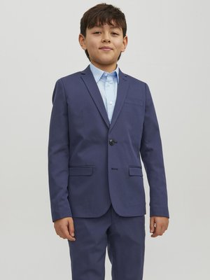 Costume bleu marine avec fermeture à un bouton, deux poches avant et pantalon assorti. Chemise bleu clair en dessous, texture de tissu lisse.