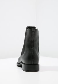 Black leather ankle boots with elastic side panels, a smooth texture, and a stacked heel. Rear view shows seam detailing.