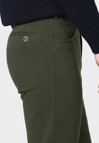 Pantalons vert olive en tissu mélange de coton, avec une coupe classique, des poches arrière et un détail distinctif de bouton doré.