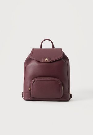 Sac à dos en cuir violet foncé avec une poche avant zippée, une poignée supérieure et une fermeture à fermoir doré sur un rabat.