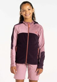Fleecejacke mit rosa und dunkelvioletten Abschnitten, mit durchgehendem Reißverschluss und orangefarbenem Reißverschlussanhänger. Kombiniert mit rosa Shorts, die Taschen haben.