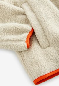 Veste en polaire crème avec des finitions orange. Dotée d'une surface douce et texturée et d'un design décontracté avec fermeture à zip.