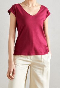 Burgundy cotton t-shirt with a v-neck and short sleeves, paired with high-waisted cream trousers, featuring a relaxed fit and smooth texture.