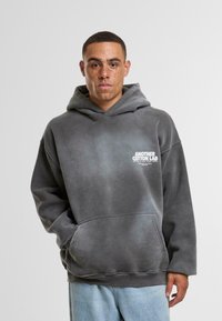 Bawełniana bluza z kapturem w gradientowym ciemnoszarym kolorze, z kieszenią typu kangur oraz białym nadrukiem logo na klatce piersiowej. Miękka tekstura i luźny krój.