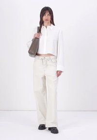 Cropped white shirt with long sleeves, paired with wide-leg beige pants. Model carries a grey handbag and wears black platform shoes.