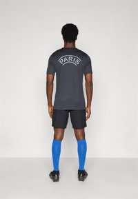 Black athletic shirt with "PARIS" logo, black shorts, and blue knee-high socks. Smooth fabric, sporty design with functional footwear.