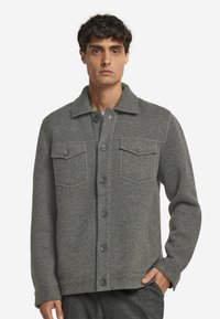 Grå ulljacka med knappframsida, två bröstfickor och en krage. Har strukturerad tyg och en rak skärning.