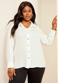 Weißes Hemd mit Knopfleiste aus einem weichen Stoff, mit Kragen, silbernen Knöpfen und langen Ärmeln, kombiniert mit schwarzen Leggings.