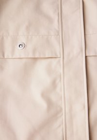 Ljusbeige tyg med en diagonalt mönster, med en framträdande knappdetalj och en ren, strukturerad design.