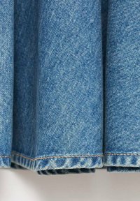 Tissu en denim bleu avec des coutures visibles le long de l'ourlet, tombant en douces plis sur un fond clair.