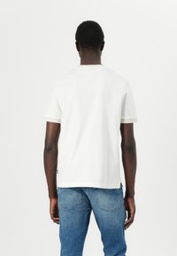 Camiseta blanca de manga corta con ribete en un suave beige claro en los puños y el cuello. Material de algodón suave, diseño clásico de cuello redondo, ajuste casual.