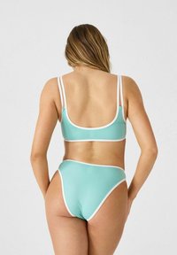 Conjunto de bikini verde menta con acentos blancos. La parte superior cuenta con tirantes delgados y una espalda baja; parte inferior de talle alto con un diseño de pierna alta.