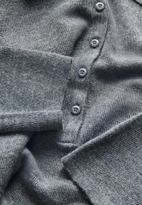 Šedá pletená vesta s žebrovanými manžetami a pěti shodnými knoflíky seřazenými vertikálně na přední straně.