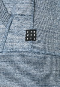 Hoodie blu con effetto heathered e finitura testurizzata, con un'etichetta nera con testo bianco "DNM WORKRS" cucita nella cucitura laterale.