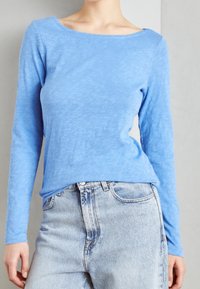 Jasnoniebieska bluzka z długim rękawem wykonana z miękkiego, teksturowanego materiału z okrągłym dekoltem, połączona z dżinsami o wysokim stanie w jasnym odcieniu.
