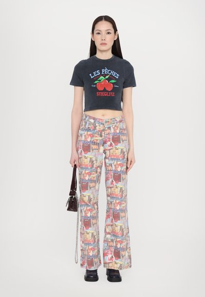 Cropped dark gray T-shirt with red cherry graphic; flared pants featuring a collage print; handbag with chain strap; chunky black footwear.