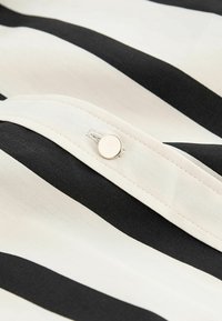 Gros plan d’un tissu rayé noir et blanc avec un poignet blanc fixé par un petit bouton rond blanc.