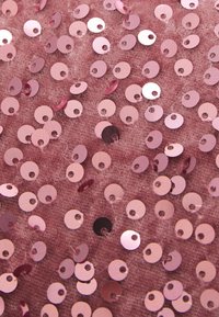 Rosa paljettyg med cirkulära paljetter i olika storlekar, vissa blanka och andra matta, på en mjuk, strukturerad bakgrund.