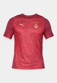 Piros rövid ujjú sportpóló, texturált mintával, arany Puma logóval és három csillagos klub címerrel.