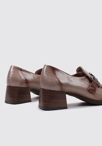 Chaussures en cuir marron à talons blocs avec une finition texturée et une sangle décorative avec quincaillerie. Design bas et forme de bout arrondi.