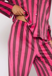 Roze en donkerbruine gestreepte pyjama set met een knoopsluiting shirt en broek met elastische tailleband, gemaakt van zachte, fluweelachtige stof.